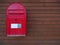 A new red mailbox with dark brown wooden background.