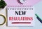 New Regulations text written on a notebook with pencils, magnifier