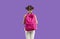 New roomy pink school backpack on back of little girl, isolated on purple background.