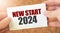 NEW START 2024 word inscription on white card paper sheet in hands of a businessman