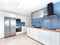 New stylish bright kitchen with white cabinets and blue tiles. Spacious modern fully equipped appliance interior with wooden desk