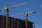 New tall residential building construction site in the city with cranes and scaffolding, blue sky background .