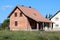 New unfinished small red brick family house with front porch surrounded with uncut grass and other houses