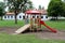 New vintage looking outdoor playground equipment in shape of slide and rope climbing with abandoned military barrack in background