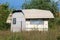 New white camper trailer parked in backyard and covered with protective nylon sheet surrounded with wire fence and high grass