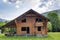 New wooden ecological cottage with balcony, terrace, steep roof from natural materials under construction on grassy meadow on fore