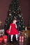 New Year 2020! Merry Christmas, happy holidays! A little girl in a red dress sits on a chair in a beautifully decorated New Year`s