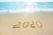 New Year 2020 on the sandy shore against the backdrop of sea waves. Beautiful sunrays illuminate the inscription 2020 on the sand