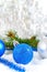 New Year background with blue and silver Christmas balls in snow, spruce green branches on light background.