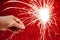 New Year celebration. Womans hand holds bright sparkler on red background. Christmas night. Bright sparks of fire and