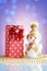 New Year / Christmas gift in package, golden beads and Snowman toy on a glass table with a beautiful blue bokeh