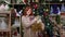 New Year sale, portrait of joyful woman with gifts in her hands near shelves with goods background of Christmas tree