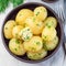 New young boiled potato topped with melted butter and chopped dill in ceramic bowl, square format, top view