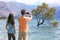 New Zealand tourists taking phone pictures of Wanaka Lone Tree at lake. People looking at view of famous touristic