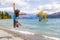 New Zealand travel happy tourist woman jumping of joy at Wanaka lake landscape with lone tree, famous attraction