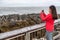 New Zealand travel tourist girl taking smartphone pictures with phone app at Punakaiki Pancake Rocks. Woman in Paparoa National