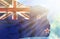 New Zealand waving flag against blue sky with sunrays