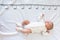A newborn 2 month baby in white sleeps on a bed on which a measuring ruler for growth is drawn