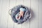 Newborn baby boy wrapped in blue wrap on gray furry blanket in white basket and with blue woolen crown headdress on white wood flo