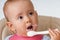 A newborn baby with a dirty face eats cottage cheese with a spoon on his own, close up