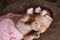 Newborn baby girl sleeping cute, covered with soft pink scarf, neatly folded under a pen with a small head with a pink bow, set