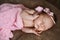 Newborn baby girl sleeping cute, covered with soft pink scarf, neatly folded under a pen with a small head with a pink bow, set