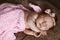 Newborn baby girl sleeping cute, covered with soft pink scarf, neatly folded under a pen with a small head with a pink bow, set