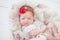 Newborn baby girl in a white lace bodysuit and a bandage with a red flower looks in the frame, smiling newborn baby