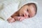 Newborn baby lies on a white plaid, covered with a knitted shawl