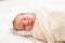 Newborn baby with milia on face sleeping swaddled in blanket