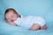 Newborn baby sleeping on his tummy full length side profile blue background