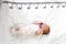 A newborn baby in white sleeps on a bed on which a measuring ruler for growth is drawn