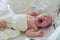 Newborn baby yawns hiding behind his hand. The baby, covered with a white diaper, wakes up. The child blinks yawning. The