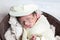 newborn cute boy covered with towel and cap sleeping in wooden round bowl decorative tiny props and flowers