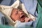 Newborn, eyes closed, crying baby in green blanket in hospital