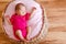 Newborn girl in pink bodysuit barefoot lies in round crib and sleeps