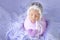 A newborn girl sweetly sleeping in a cocoon on a lilac background fur in a beautiful cap, art photo of a newborn baby
