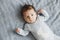 Newborn pretty baby boy in blue sleepwear lying on grey sheet, top view