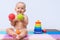 Newborn sits on the floor and plays with a green and red rubber ball