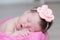 Newborn sleeping in basket with knitted flower on head, baby girl lying on pink blanket, cute child
