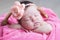 Newborn sleeping with knitted flower on head. Infant baby girl closeup lying on pink blanket in basket. Cute portrait of child