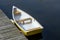 Newer yellow and white rowboat sits moored on a calm quiet harbr