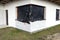 A newly applied layer of white silicone plaster on the wall of the house, the cornr window and door are secured with black foil.