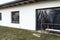 A newly applied layer of white silicone plaster on the wall of the house, visible metal scaffolding and boards, window is secured