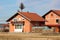 Newly built unfinished red brick family house with new roof tiles surrounded with dry grass and stacked firewood