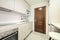Newly installed kitchen with smooth white cabinets without handles, white stone conglomerate worktop and light laminated flooring