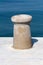 Newly made dark grey concrete mooring bollard looking like mushroom on top of concrete pier with calm clear blue sea in background