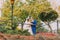 Newly married couple posing in sunny park near handrail. Groom is gently holding his elegant bride