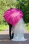 Newly-married couple under a pink umbrella