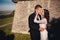 Newlywed couple posing near old castle wall, fairytale wedding at ancient castle outdoors, bride and groom hugging near fortress